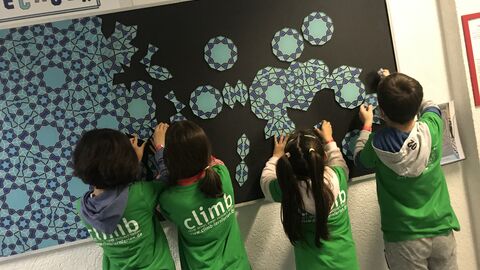 Kinder in grünen "climb"-Shirts kleben Mosaikteile an eine Tafel.