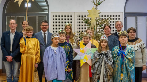 Eine Gruppe Sternsinger mit Ministerpräsident Rhein und Staatsminister Wintermeyer in der Staatskanzlei, sie halten Schilder in der Hand