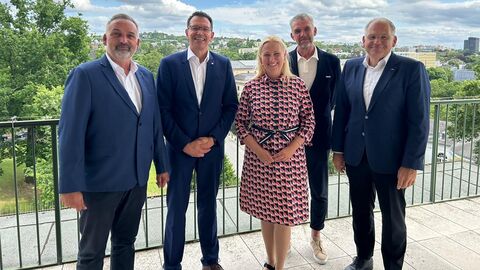 Gesundheitsministerin Stolz steht mit weiteren Personen zusammen, im Hintergrund ein Geländer und blauer Himmel.