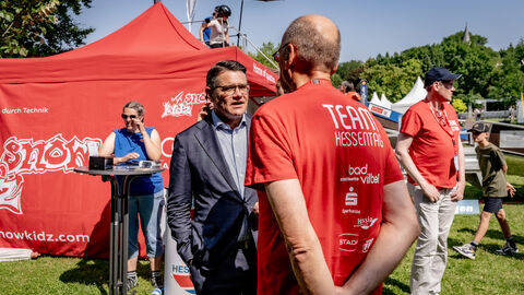 Ministerpräsident Boris Rhein spricht mit einer Person in einem roten T-Shirt