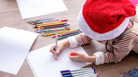 Ein Mädchen mit Weihnachtsmann-Mütze malt mit Buntstiften auf weißem Papier.