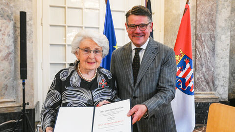 Eine Frau und ein Mann stehen nebeneinander und halten eine Urkunde hoch.