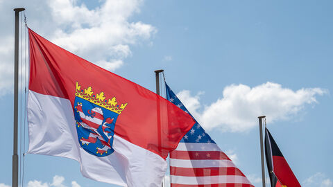 Die Flagge von Hessen, USA und Deutschland wehen nebeneinander an einem Fahnenmast und ragen in den Himmel.