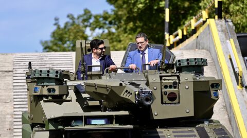 Zwei Personen sitzen in einem Panzerfahrzeug. 