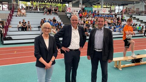 Martina Schneider, kooptiertes Präsidiumsmitglied Special Olympics Hessen, Innen- und Sportminister Peter Beuth und Kultusminister Prof. Dr. R. Alexander Lorz stehen auf einer Tartanbahn ihn einem Sportstadion. Im Hintergrund Kinder in Sportkleidung.