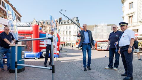 Innenmnister Beuth steht auf einem großen Platz und wirft Kugeln über ein Geländer, daneben weitere Personen.