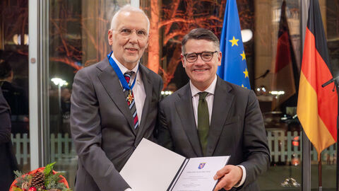 Zwei Männer lachen in Kamera und halten Ehrung in den Händen.