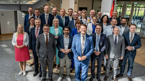 Das Hessische Kabinett mit Bad Vilbels Bürgermeister Sebastian Wysocki auf dem 62. Hessentag in Bad Vilbel. 27 Männer und Frauen stehen in Anzügen und Hosenanzügen in einer Eingangshalle.