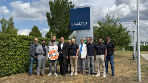 Mehrere Personen stehen auf einer Wiese und schauen in die Kamera. Hinter ihnen ist das Logo des Unternehmens Scaltel zu sehen